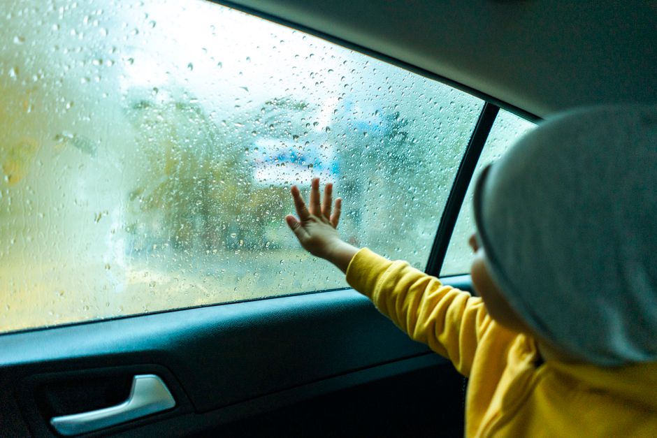 雨滴のある車の窓に触れる子供、雨の中のドライブでの好奇心と驚きを伝えています。
