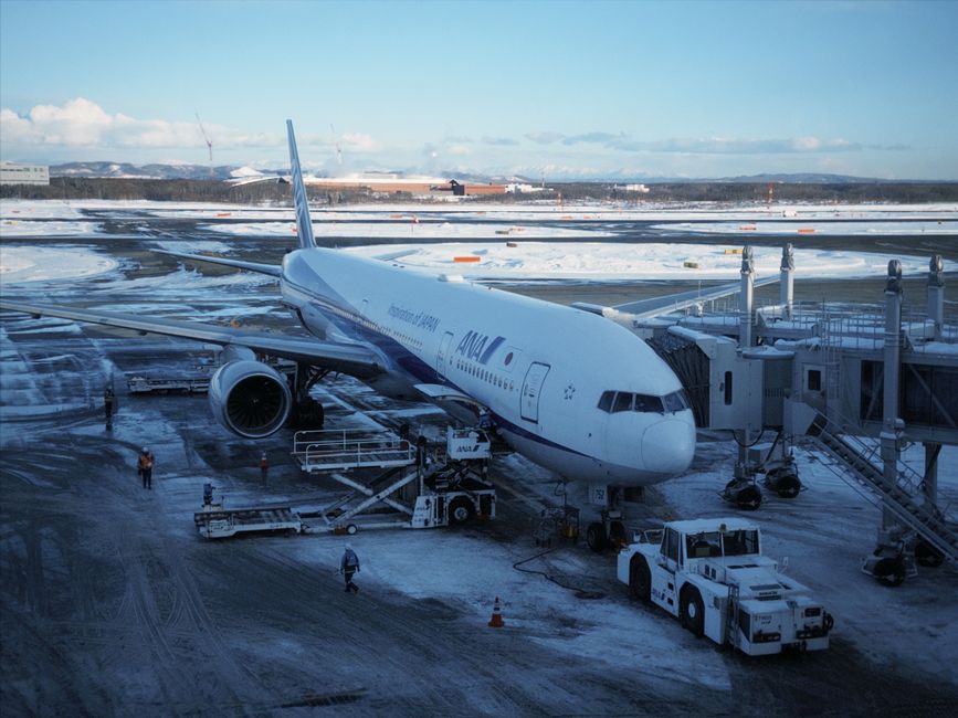 冬の新千歳空港に駐機している飛行機。雪と地上要員に囲まれている。