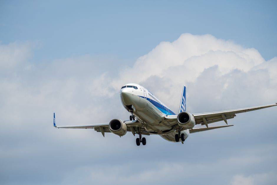 青い空とふわふわの雲を背景に上昇する商業航空機で、世界旅行を表現しています。